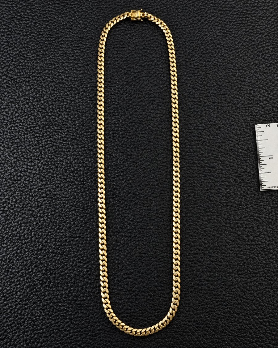 A gold Miami Cuban link chain laid flat on black leather beside a ruler