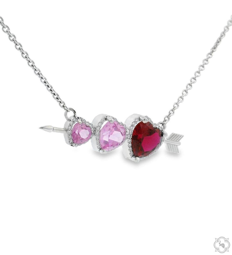Silver necklace with three heart-shaped pink and red gemstones on an arrow pendant