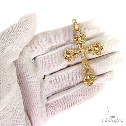 Yellow gold cross pendant with intricate filigree and diamond accents held by gloved hand
