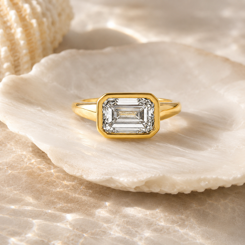 Yellow gold ring with emerald-cut diamond in bezel setting on shell background
