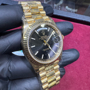 18K yellow gold Rolex Day-Date 40mm watch with black stick dial and fluted bezel.