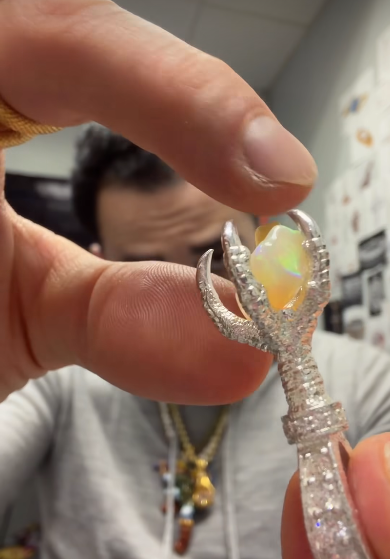 Silver eagle claw pendant with opal gemstone and diamond accents, held between fingers