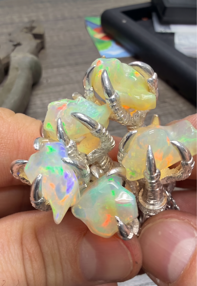 Silver eagle claw pendants holding luminous free form opal gemstones with iridescent flashes