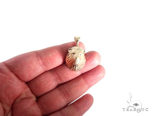 Small yellow gold lion head pendant with detailed mane and ruby red eyes held in hand