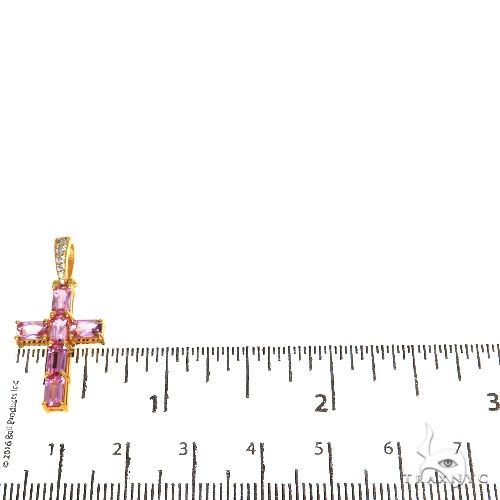 Rose gold cross pendant with pink emerald cut sapphires and diamond accents, next to ruler