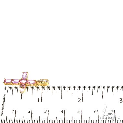 Pink emerald cut sapphire cross pendant with yellow gold bail, shown next to ruler for size