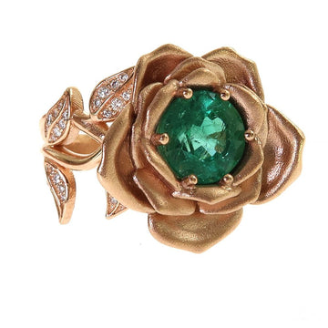 Rose gold floral ring with emerald center stone and diamond-accented leaves.