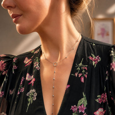 Sterling silver lariat necklace with delicate chain and small bead accents, worn with floral dress.