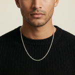 Man wearing a black sweater with a silver chain necklace against a beige background