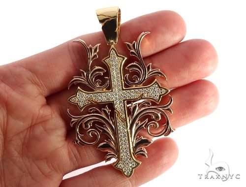 14k two-tone gold cross pendant with diamond filigree details held in hand