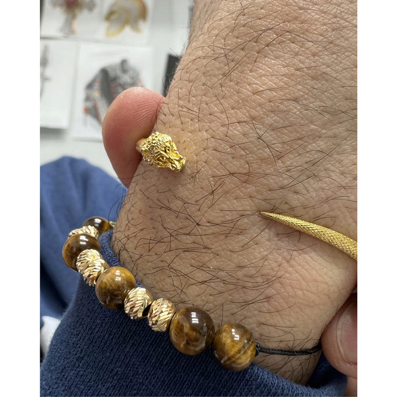 24K gold snake ring with detailed head design on wrist above tiger eye bead bracelet.