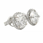 Round white gold diamond stud earrings with halo design and brilliant cut stones.