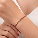 Yellow gold tennis bracelet with round ruby gemstones and secure clasp closure.