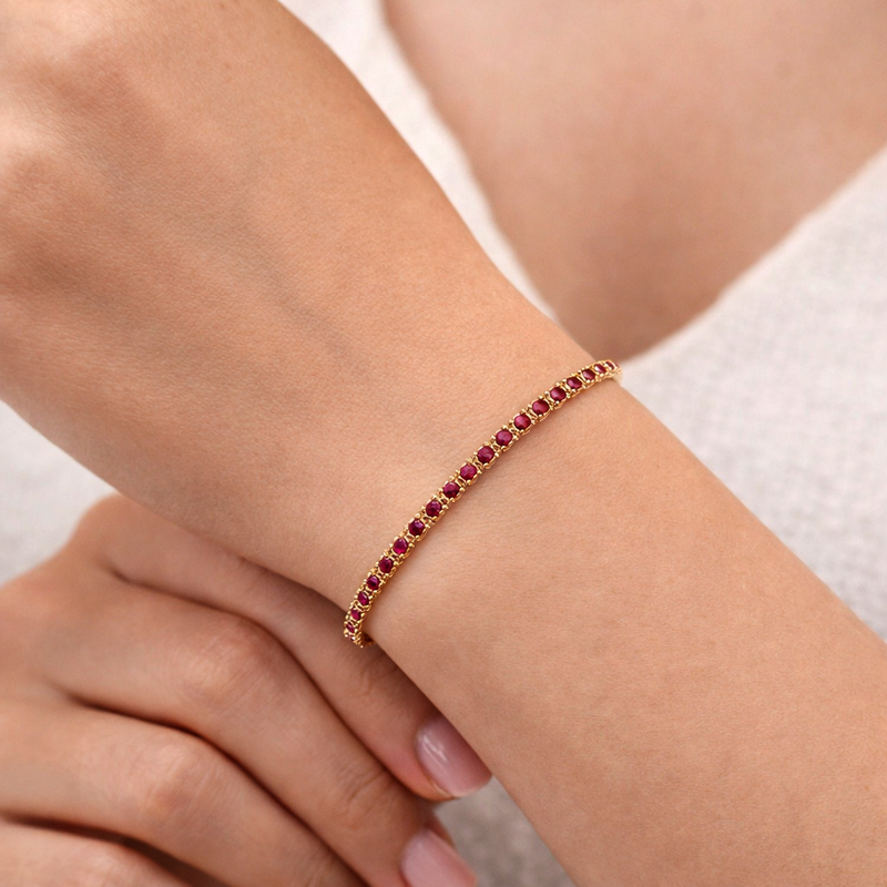 Yellow gold tennis bracelet with round ruby gemstones and secure clasp closure.