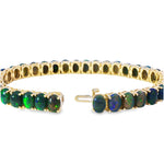 Gold tennis bracelet featuring oval black opals with vibrant green and blue hues.