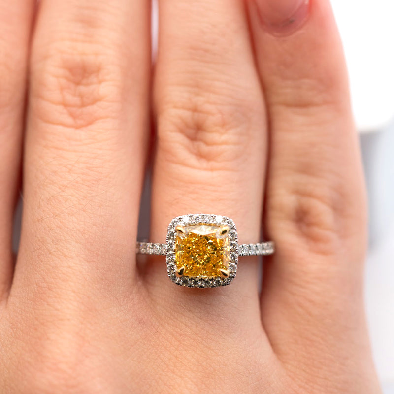 Cushion-cut yellow diamond ring with halo of white diamonds on a white gold band.