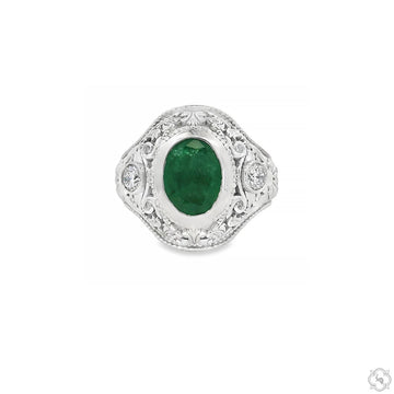 Silver ring with oval green emerald center and intricate filigree detailing.