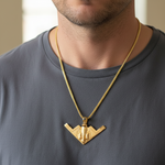 Gold B-2 bomber pendant necklace on a fine gold chain, worn on a gray shirt.