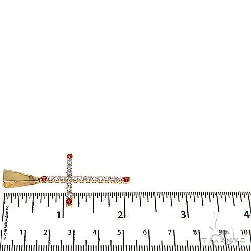 Diamond cross pendant with red accents displayed on white measuring tape in inches