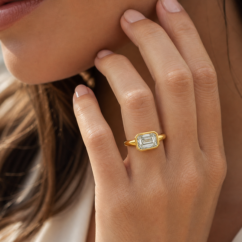 Yellow gold ring with bezel-set emerald cut green center stone on finger