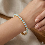 Gold tennis bracelet with oval opal gemstones on a wrist, unisex design.