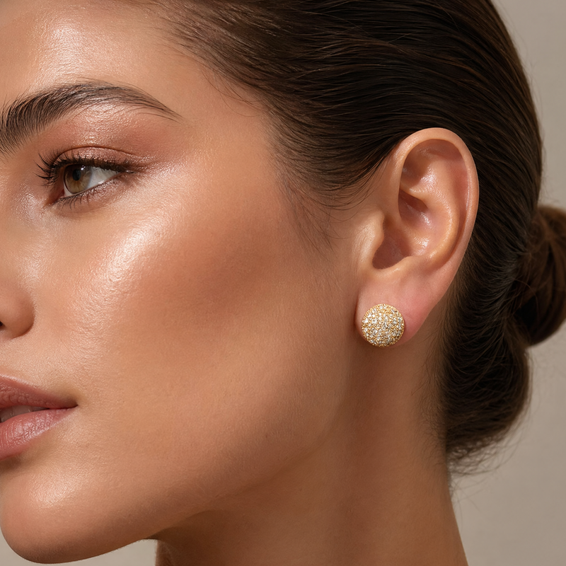 Gold round stud earrings with small diamond pavé, worn on a woman's ear