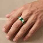 Gold band ring with alternating rectangular emerald and white opal stones on hand.