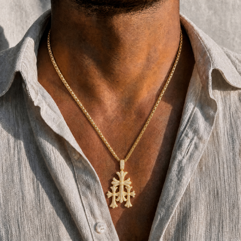 Gold triple cross pendant with intricate design on a matching gold chain, worn with a linen shirt.