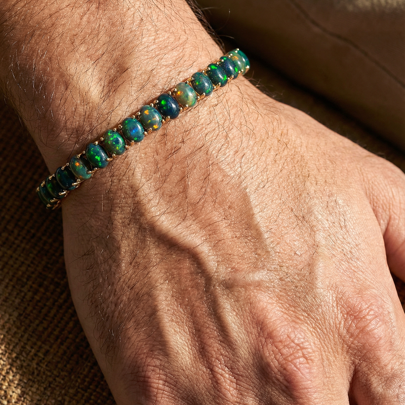 Gold tennis bracelet with oval galaxy black opal gemstones on wrist.