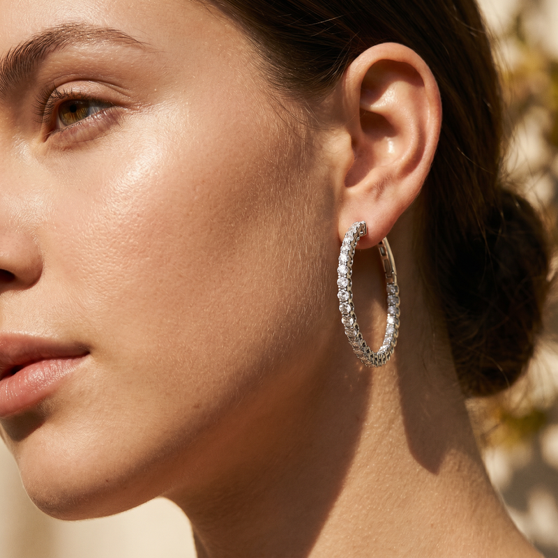 Silver inside-out diamond hoop earrings worn on a woman’s ear with a smooth polished finish.