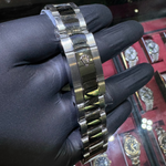 Silver watch band held by a gloved hand with a display of watches in the background