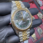 Gold and silver watch held by a gloved hand with a display of watches in the background.