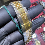 Gold and silver watch on a gloved hand with a display of watches in the background