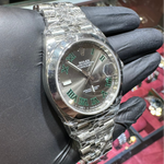 Silver watch with a detailed face held by a gloved hand against a jewelry display.