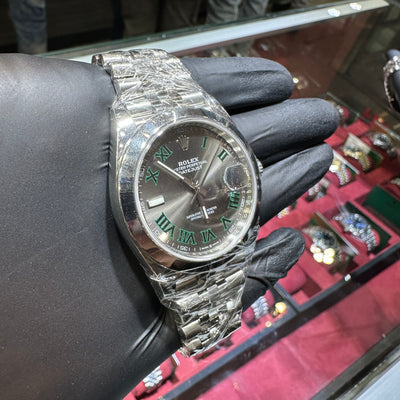Silver watch with a detailed face held by a gloved hand against a jewelry display.