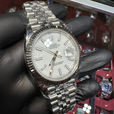 Silver watch with a detailed face held by a gloved hand against a blurred background