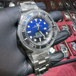 Watch with blue dial held by a gloved hand against a background of jewelry boxes.