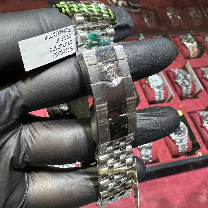 Silver watch with a detailed band held by a gloved hand, with a display of watches in the background.