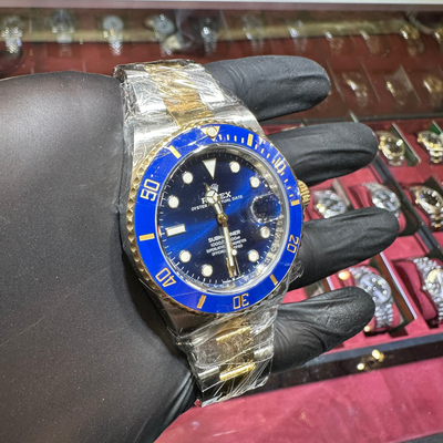 Watch with blue bezel and face held by a gloved hand against a jewelry display background
