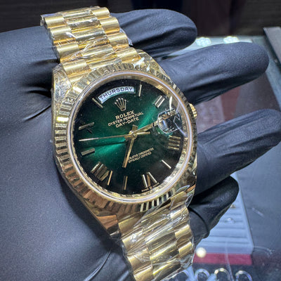 Gold Rolex watch with a green face held by a gloved hand.