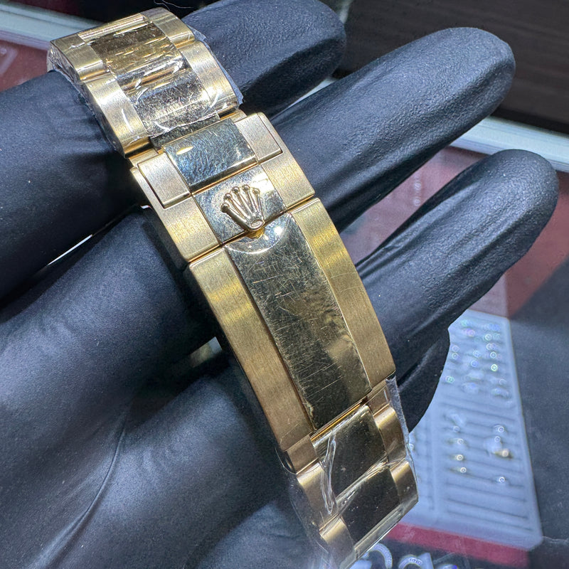 Gold watch bracelet with a visible brand logo on a black gloved hand.