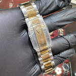Gold and silver watch band held by a gloved hand with a blurred background