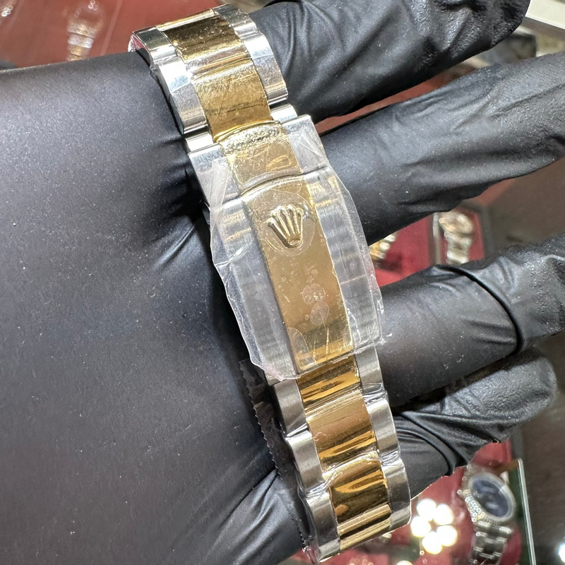 Gold and silver watch band held by a gloved hand with a blurred background