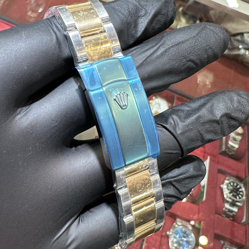 Gold and blue watch band held by a gloved hand with a jewelry store background.