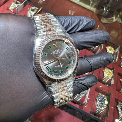 Luxury watch with green Roman numeral dial held by a gloved hand against a blurred background