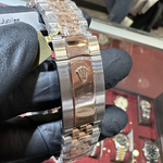 Gold and silver watch with Rolex logo held by a gloved hand, blurred background of jewelry store.