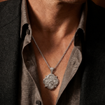 Silver anchor pendant with rope chain on a man's chest, casual open-collar shirt visible.