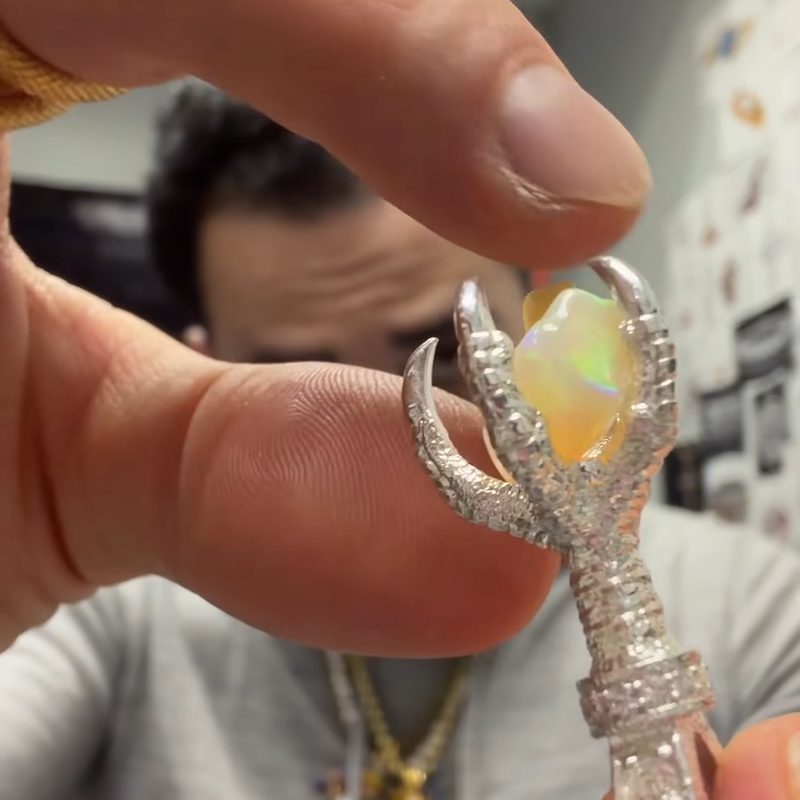 Silver eagle claw pendant with opal gemstone and diamond accents, held between fingers.