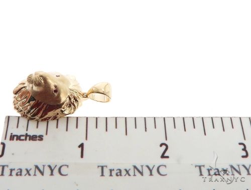 Small yellow lion head pendant with detailed mane and red ruby eyes, next to ruler for size reference