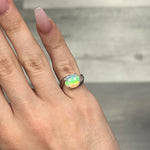 Silver pinky ring with oval opal gemstone and bypass band design.